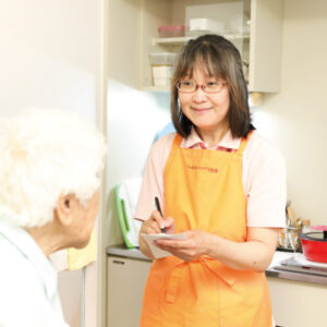 スタッフが入居者に食事を提供している様子。キッチンでの日常的ケア場面
